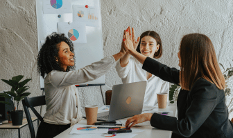 3 women high-fiving around a laptop