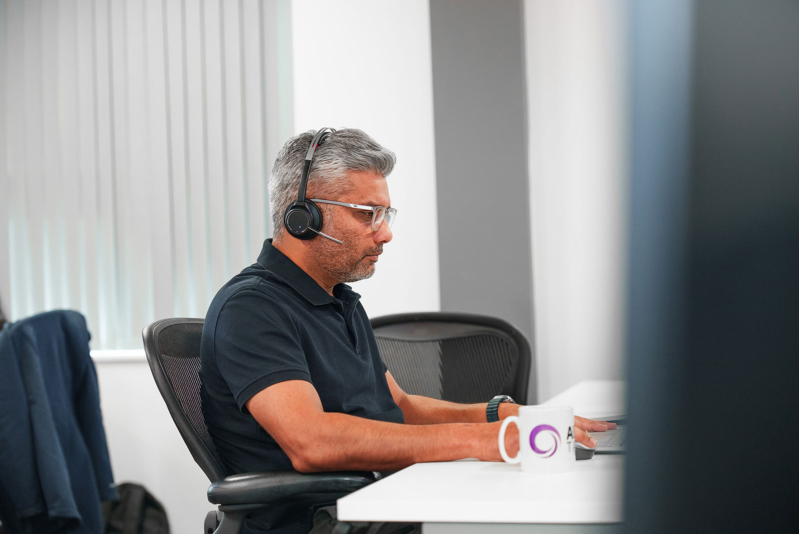 Pradeep Banda, Client Delivery Consultant, wearing a headset and working at his laptop in our office