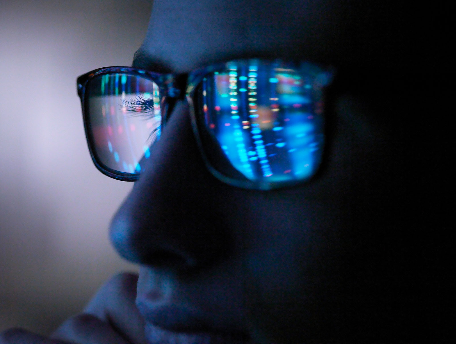 Close-up of a person wearing glasses, with glowing lines of data reflected in the lenses